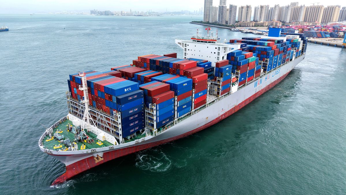 A cargo ship with containers departing from Qingdao Port, China (2025) A cargo ship with containers in front of a city skyline