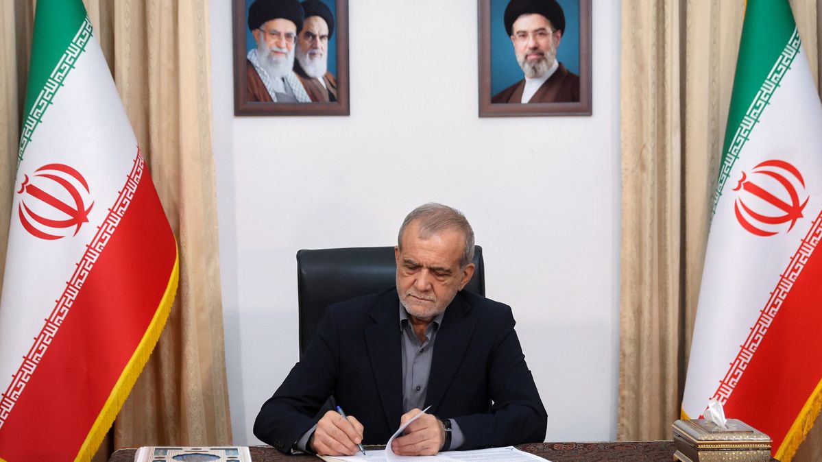Irans Präsident Masoud Pezeshkian unterzeichnet in Teheran eine Absichtserklärung zur Beendigung des Krieges. Der Präsident Irans am Schreibtisch vor zwei iranischen Flaggen