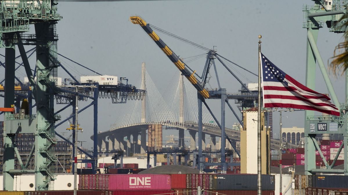 Eine amerikanische Flagge weht vor der Long Beach International Gateway Bridge. Eine US-Flagge weht vor Schiffscontainern und einer großen Brücke