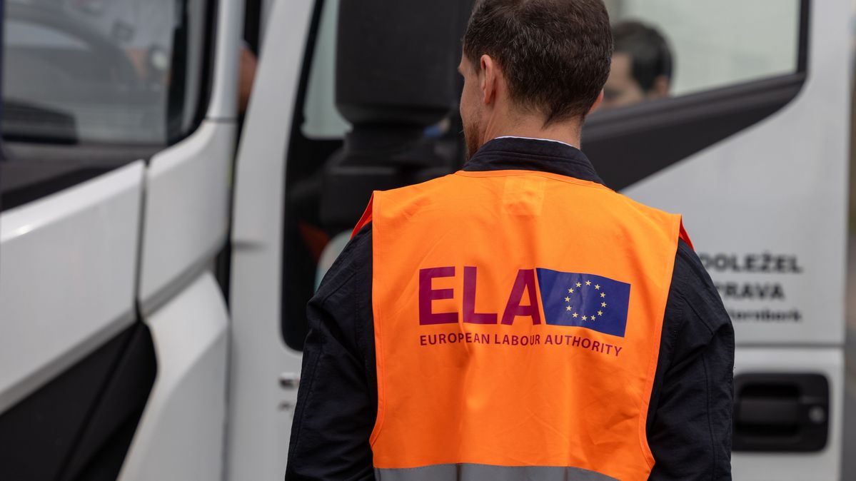 Eine Einsatzkraft der European Labour Authority steht an einer Großkontrollstelle auf der Autobahn A6 in Mittelfranken. Ein Mann mit einer orangen Warnweste mit dem ELA Logo steht vor einem LKW.