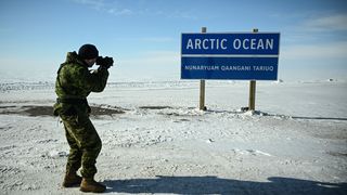 A young man photographs a sign in Tuktoyaktuk in the Arctic that reads "Arctic Ocean". 