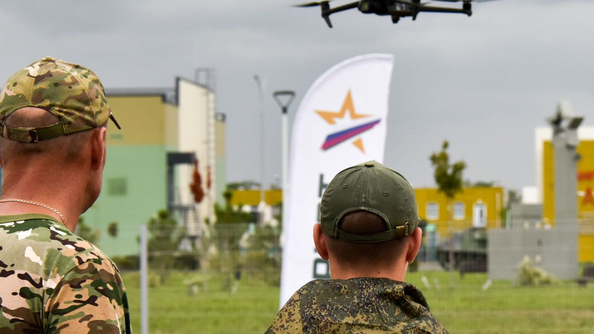A quadcopter takes flight during an open airborne training session in the Russian Dinskoy District. Two soldiers look at a flying quadcopter.