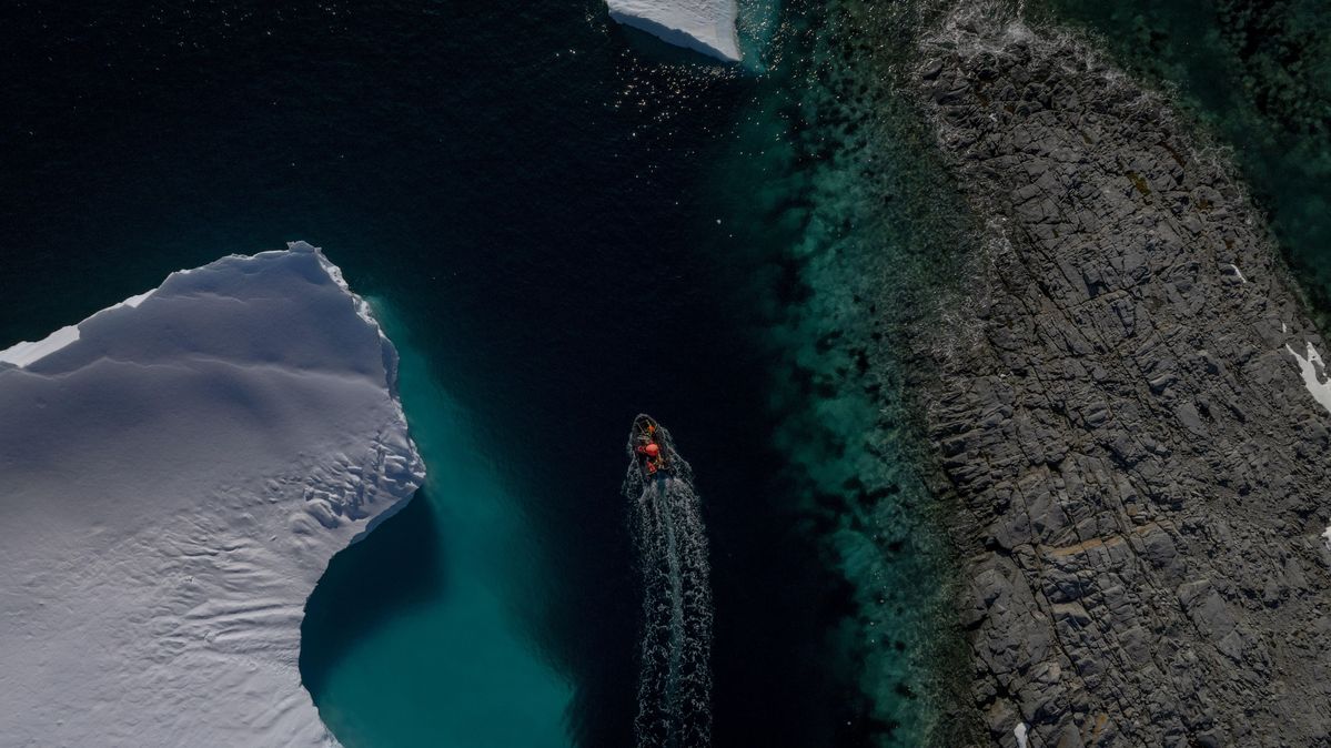 Luftaufnahme eines Gletschers in der Antarktis während einer Wissenschaftsexpedition zur Untersuchung menschengemachter Schadstoffe. Ein Schlauchboot fährt zwischen Eis und einem Felsen.